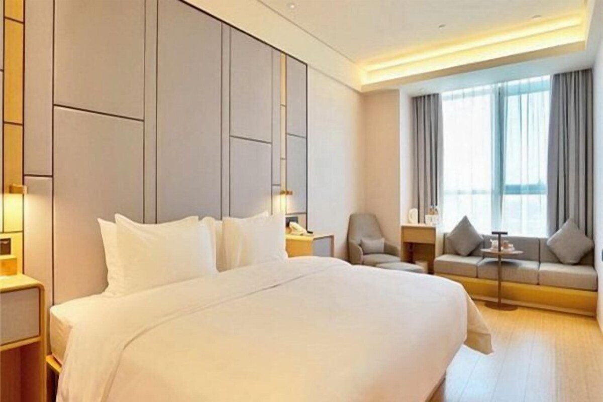 A hotel room with a large bed, a sofa, a chair, a small table, and a window with curtains.