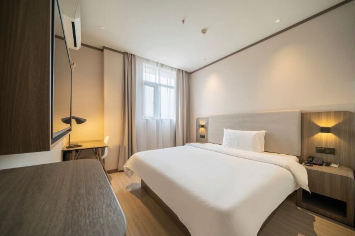 A modern hotel room with a large bed, bedside tables, a desk, and a window with curtains.