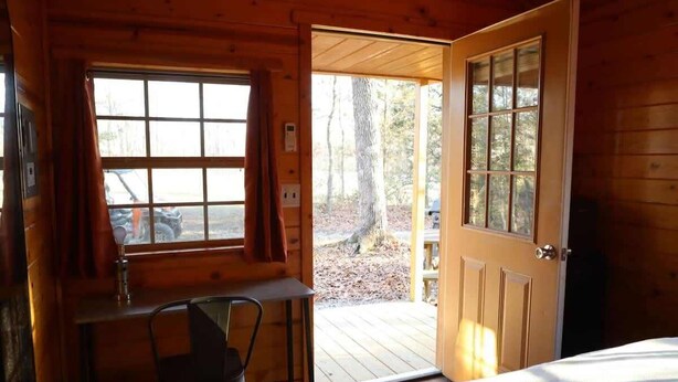 Habitación de cabaña de madera con una cama, un escritorio y una ventana con vistas a una terraza.