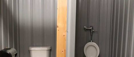 Un baño pequeño y cerrado con inodoro y orinal, paredes de metal y una viga de soporte de madera.