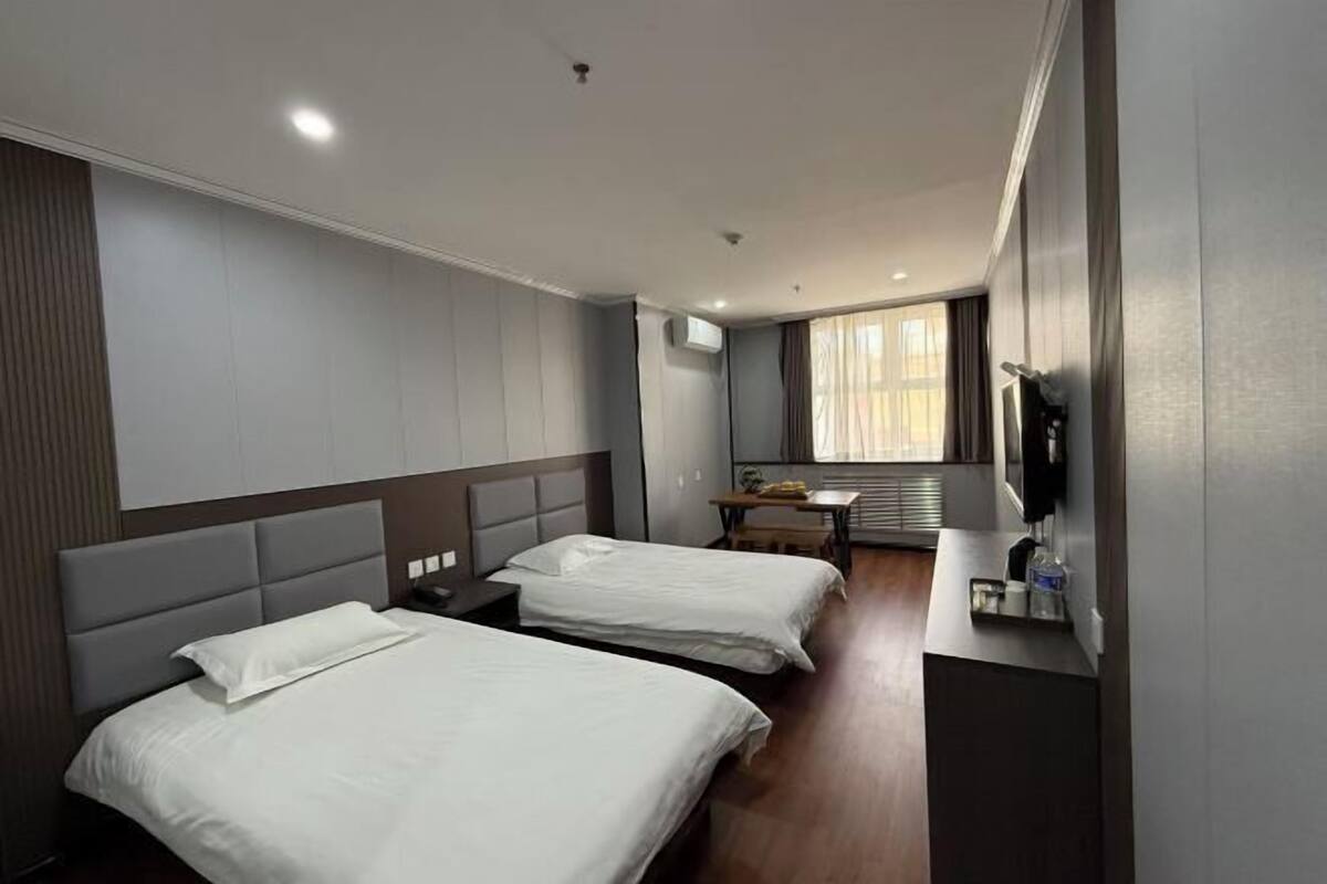A hotel room with two beds, a desk, a TV, and a window with curtains.