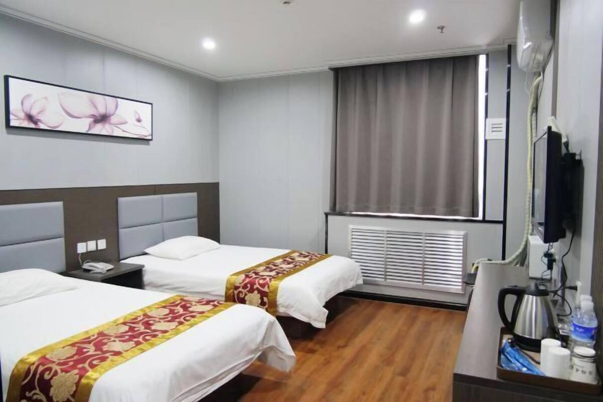 A hotel room with two beds, a flat-screen TV, a coffee maker, and a window with blinds.