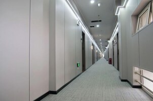 Un pasillo largo y estrecho con puertas a ambos lados, iluminación empotrada y piso de baldosas.