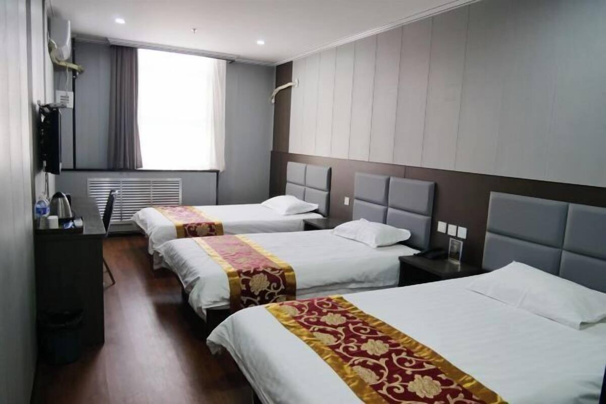A hotel room with three beds, a desk, and a window with curtains.