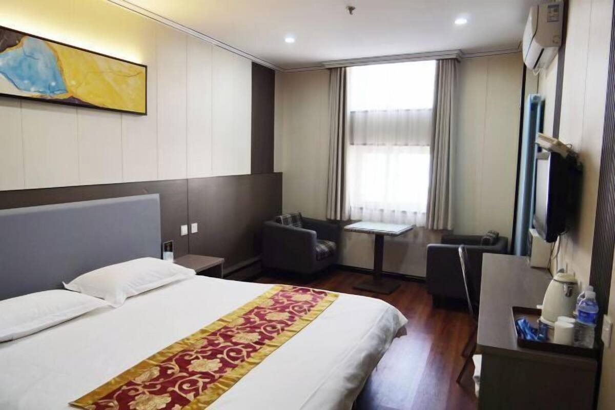 A hotel room with a bed, a desk, a chair, a television, and a window with curtains.
