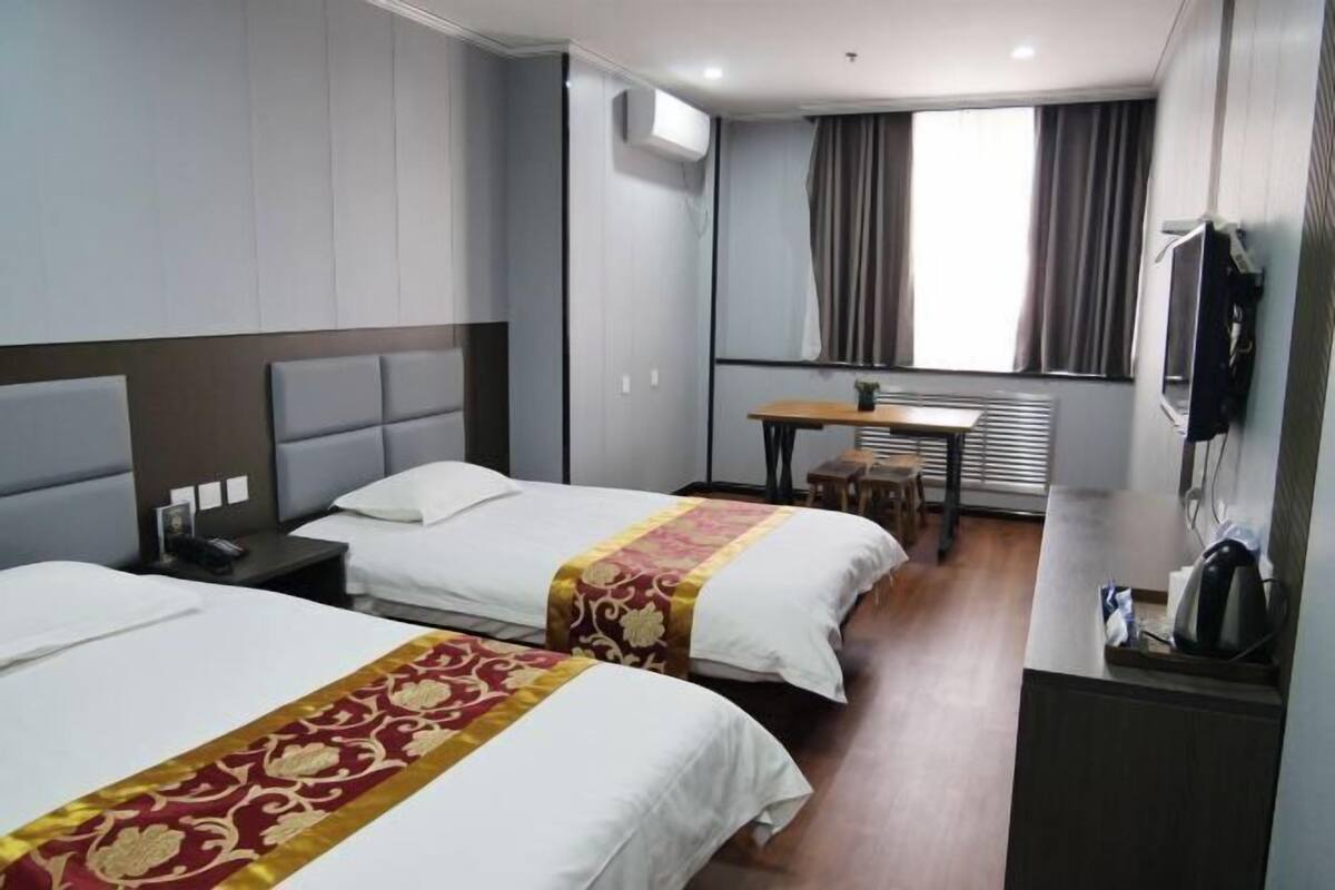 A hotel room with two beds, a small table, a TV, and a window with curtains.