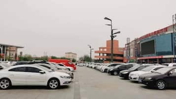 A parking lot with multiple cars parked in rows, a large building with a red facade, and a clear sky.