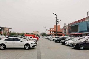 Un estacionamiento con varios autos estacionados en filas, un edificio grande de fachada roja y un cielo despejado.