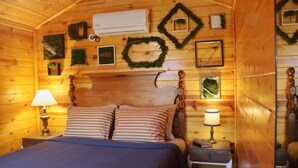 A cozy wooden cabin bedroom with a bed, two bedside lamps, a nightstand, and decorative wall hangings.