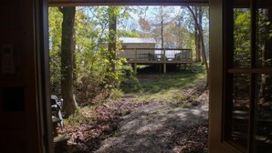 A wooden deck with a bench, surrounded by trees and a path leading to a building.