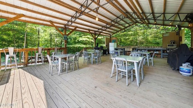 An outdoor covered patio with tables and chairs, a barbecue grill, and a view of the surrounding forest.