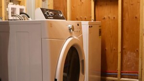 A laundry room with a front-loading washer and dryer, wooden walls, and visible electrical wiring.