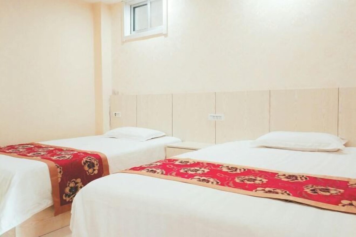 A hotel room with two single beds, each with a red floral bedspread and white pillows.