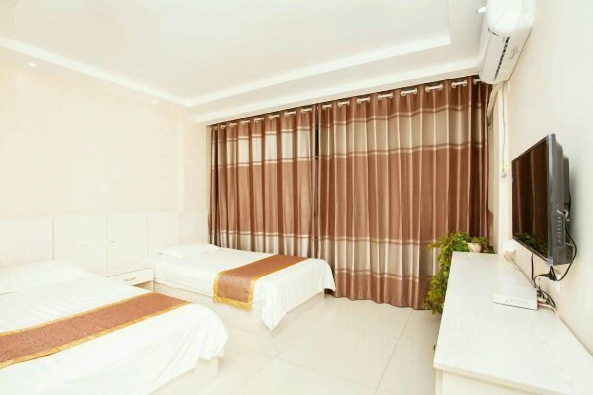 A hotel room with two beds, a TV, a desk, and a large window with curtains.