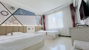 Habitació d'hotel amb dos llits, escriptori, televisió i finestra amb cortines.