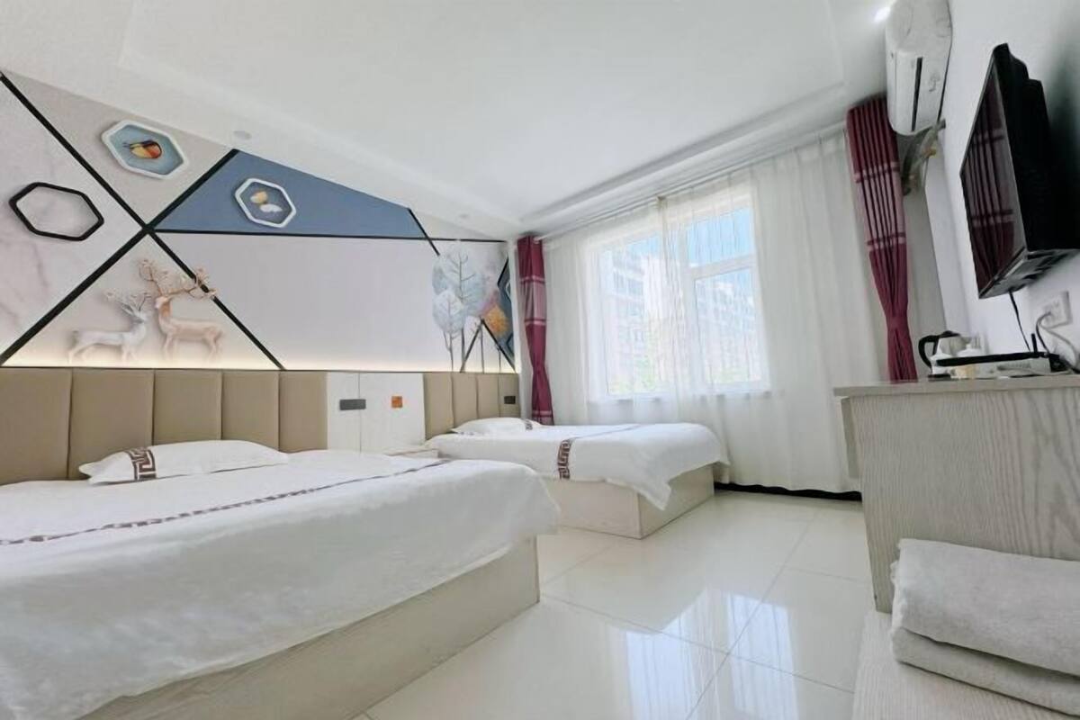 A hotel room with two beds, a desk, a TV, and a window with curtains.
