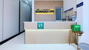 Zona d'entrada d'un hotel amb un disseny modern, que inclou un taulell de recepció, un senyal verd de sortida d'emergència i cartells informatius a la paret.