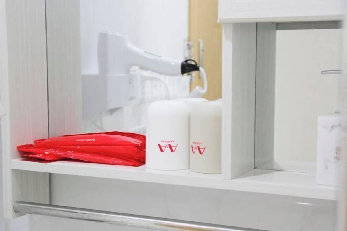 A bathroom with a white sink, a white hairdryer, and two white bottles with a logo.