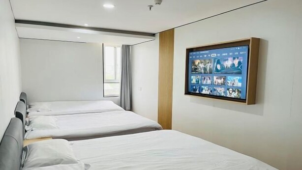 A hotel room with two beds, a large digital screen displaying various images, and a window with curtains. - AAliansuojiudian (Shanghai)