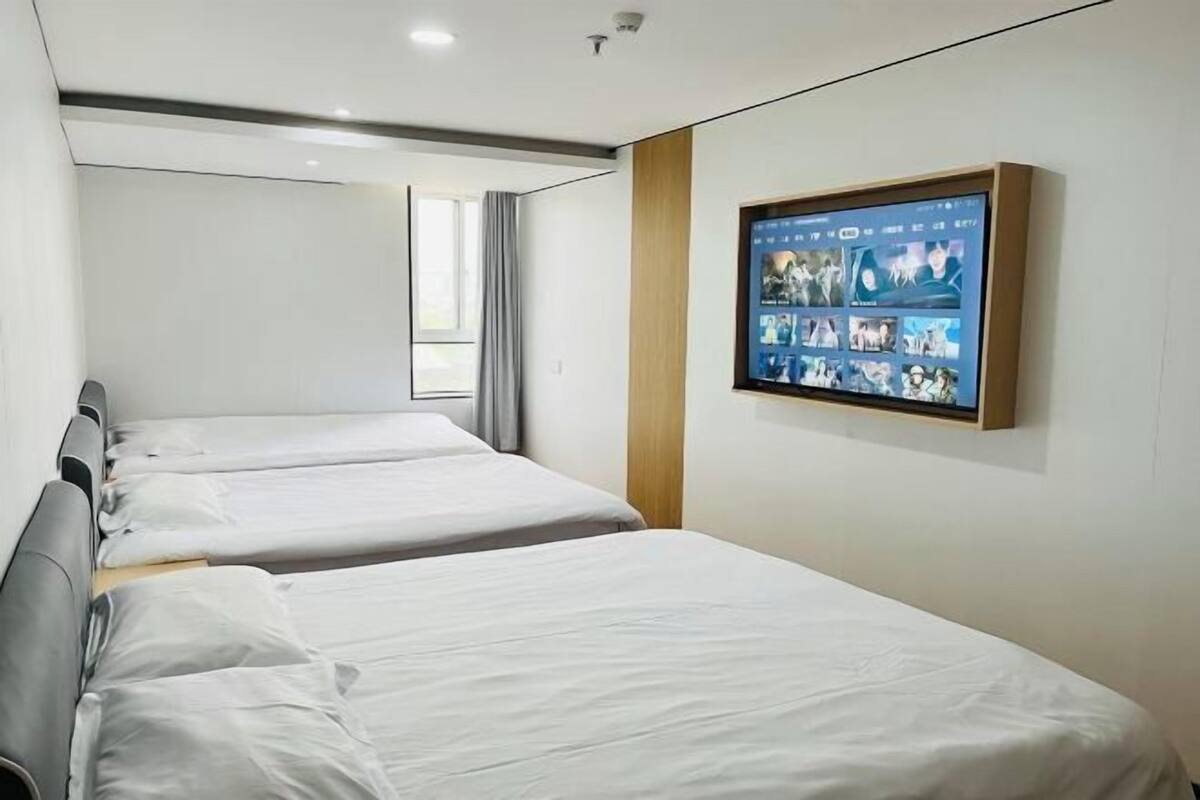 A hotel room with two beds, a large digital screen displaying various images, and a window with curtains.
