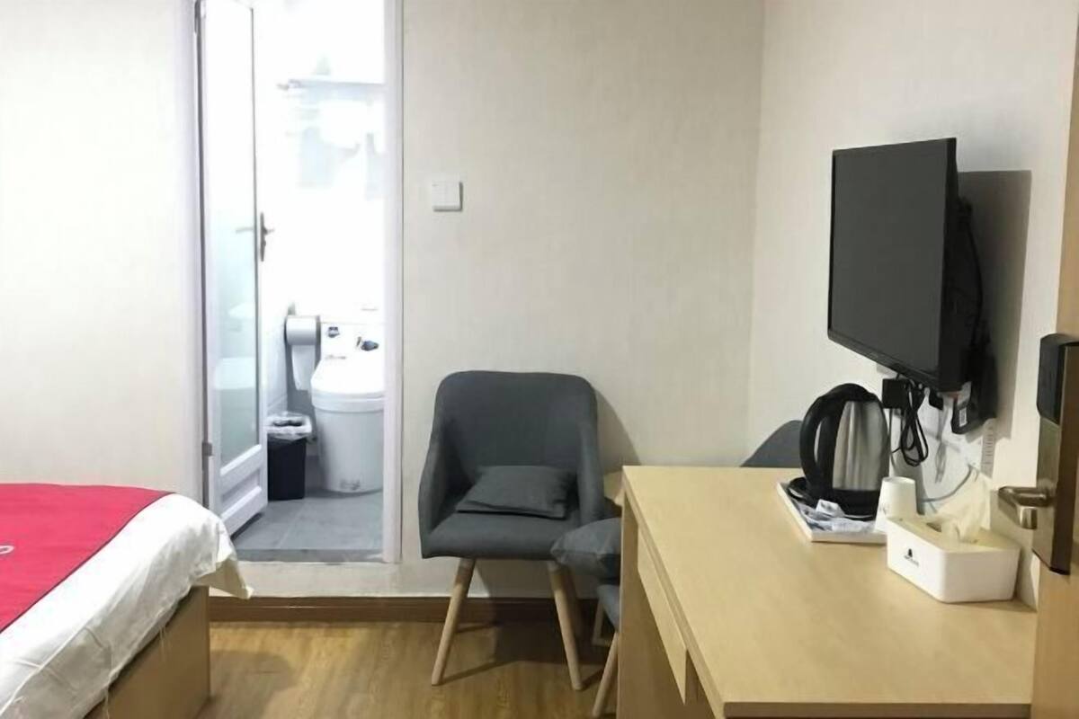 A hotel room with a bed, a desk with a television, a chair, and a window.