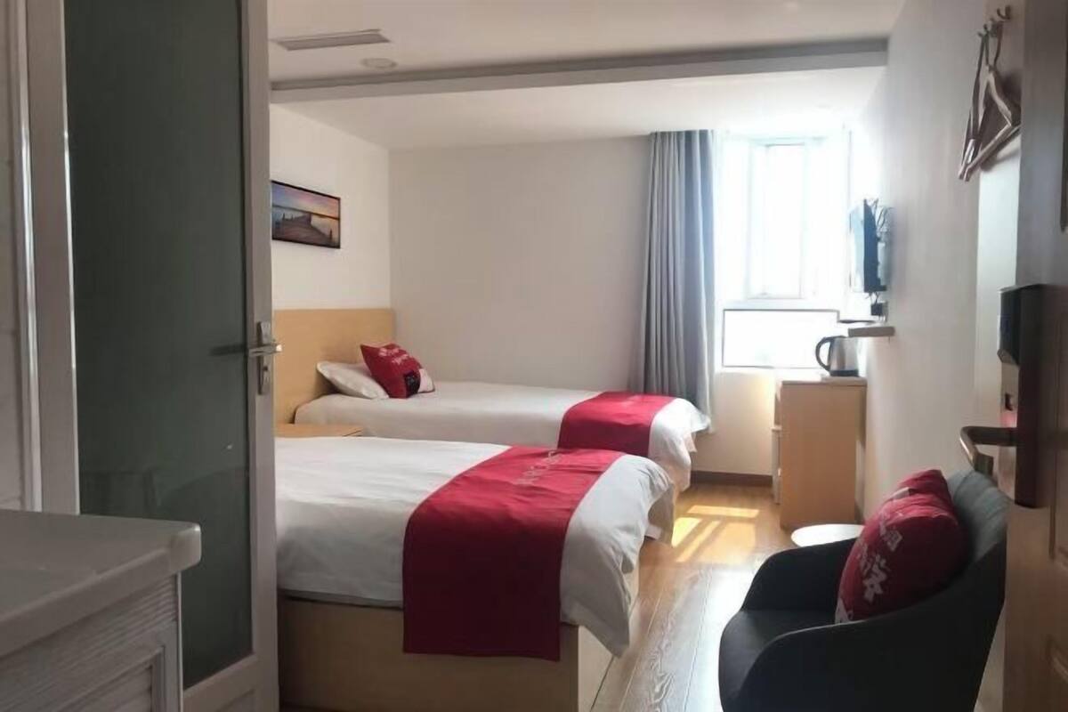 A hotel room with two beds, a desk, a chair, and a television.