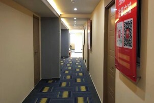A hotel corridor with patterned carpet, a red informational sign, and a door at the end.