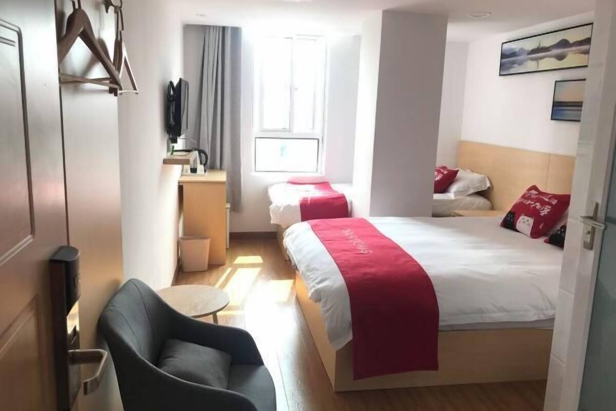 A hotel room with a bed, a chair, a small table, a TV, and a window.