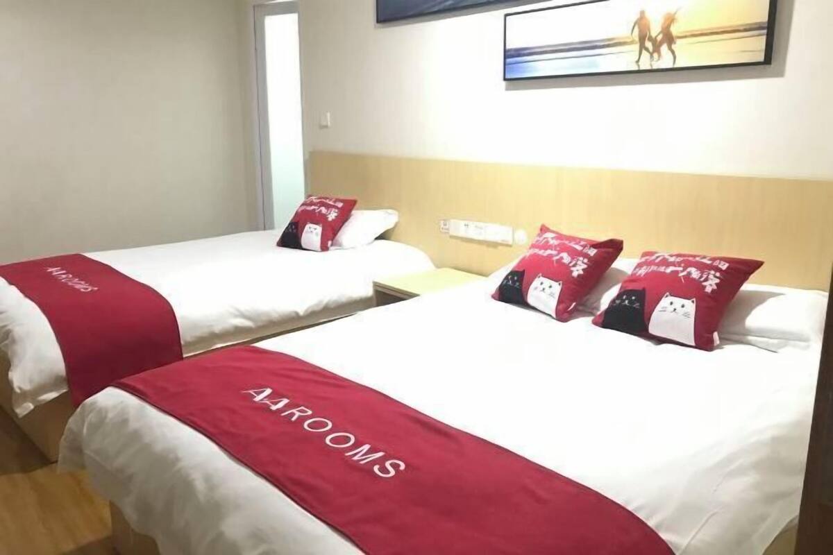 A hotel room with two beds, each with a red and white bedspread and matching pillows. The room has a wooden headboard and a painting above the beds.
