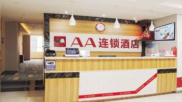 A hotel reception desk with a clock, a television screen, and a sign indicating 'AA Rooms'.