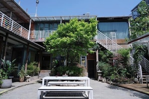 Une cour avec un banc blanc, des plantes en pot et un escalier menant à un bâtiment doté d’une façade en verre.