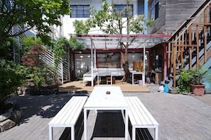 An outdoor patio area with a wooden table and chairs, surrounded by potted plants and a building with a covered seating area. - Serene Mystery Garden (Dali City)