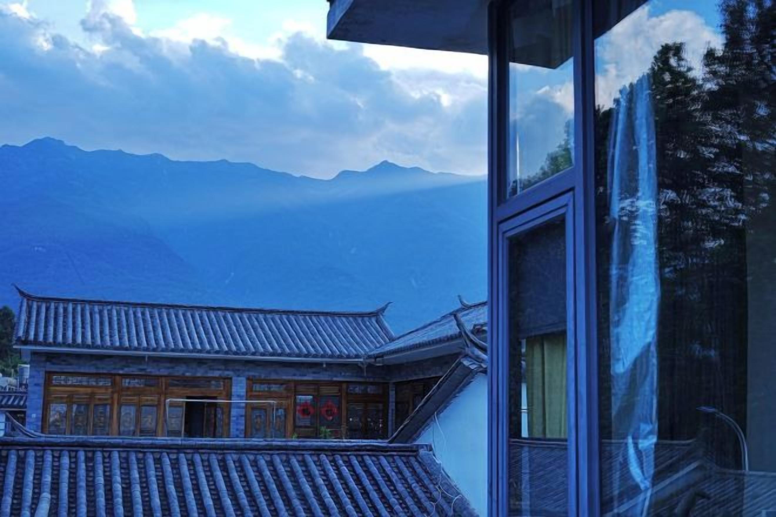 A traditional building with a tiled roof and wooden doors, viewed through a window with a reflection of trees.