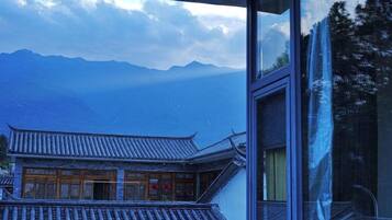 A traditional building with a tiled roof and wooden doors, viewed through a window with a reflection of trees.