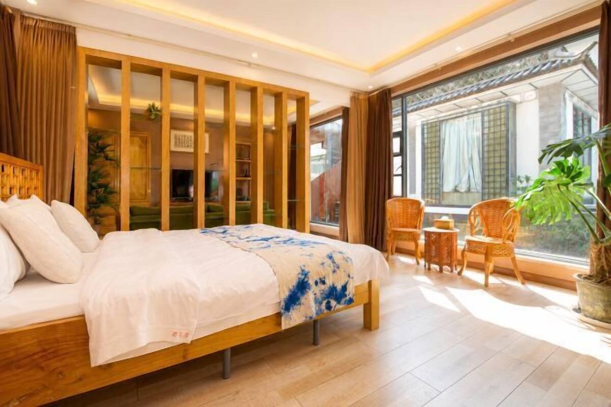 Een slaapkamer met een houten bed, een tafeltje, stoelen, een potplant en uitzicht naar buiten.