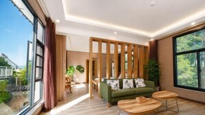 Un salon moderne avec un canapé vert, des tables basses en bois et de grandes fenêtres donnant sur un paysage verdoyant.