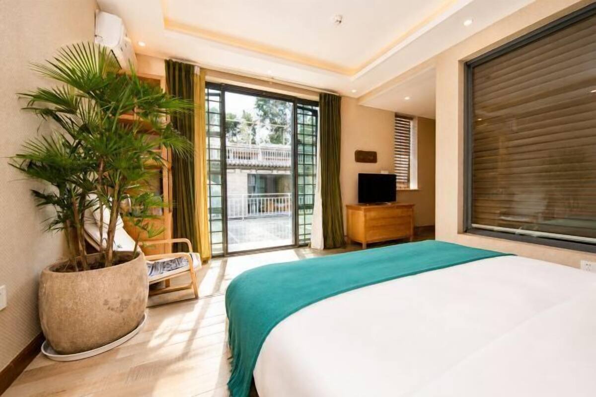 Een hotelkamer met een bed, een potplant, een televisie en een schuifdeur naar een balkon.