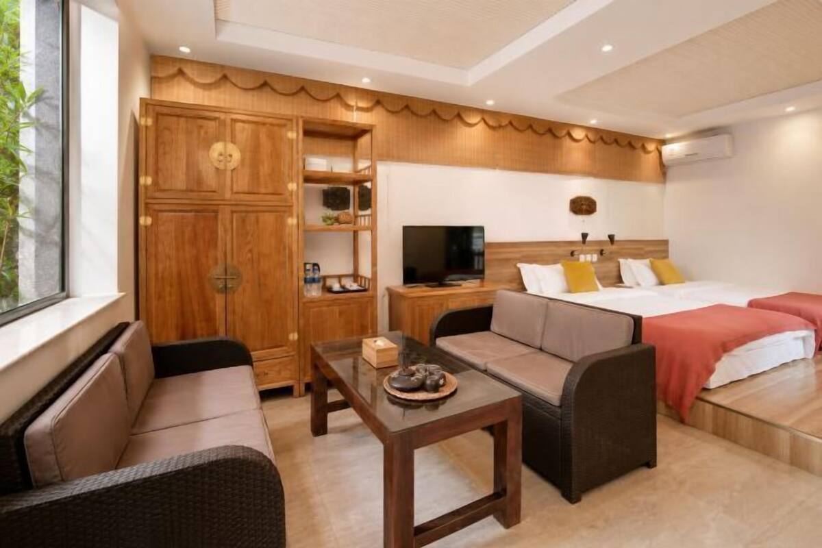 Hotelkamer met een bank, een klein tafeltje, een televisie, een bed met rode beddengoed en een houten kledingkast.
