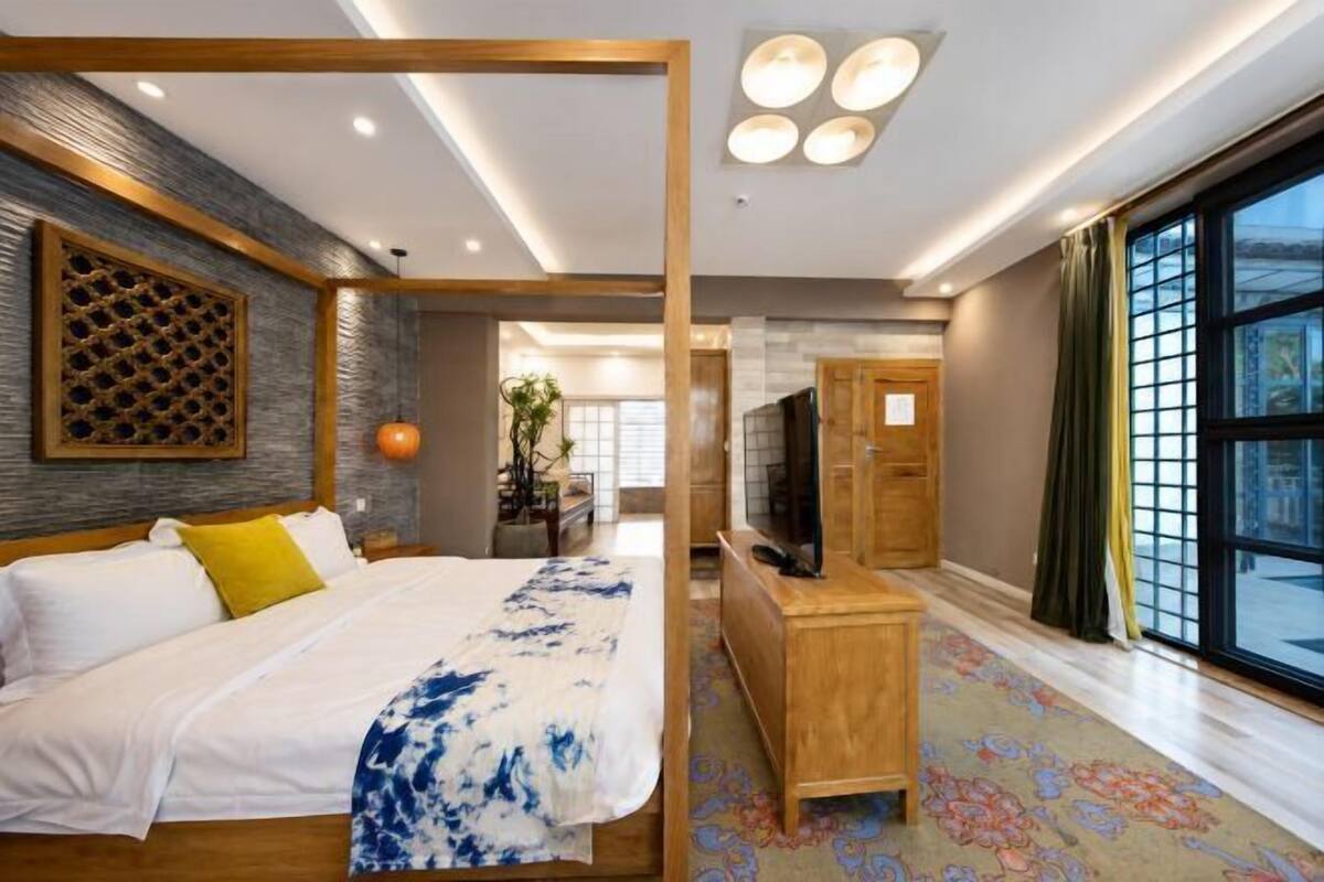 Een moderne hotelkamer met een groot bed, een houten bureau, een televisie en een ruim raam.