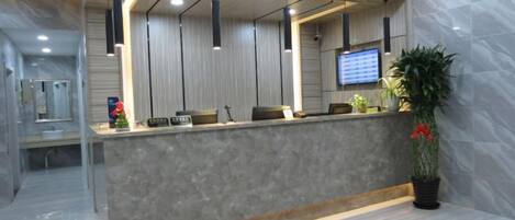 A reception area with a marble counter, pendant lighting, a television, and a potted plant.