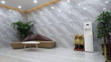 Um hall de entrada com parede de mármore, um sofá marrom, uma pequena mesa, um dispensador de água e um vaso de plantas.