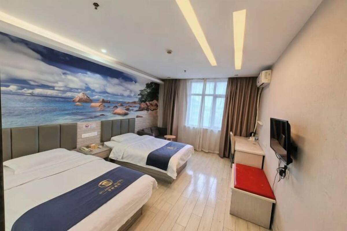 A hotel room with two beds, a desk, a TV, and a mural of a beach scene.