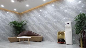A modern lobby with a marble wall, a brown leather sofa, a small round table, and a white air conditioning unit. - Thank You Inn (Shanghai Xianghuaqiao) (Shanghai)