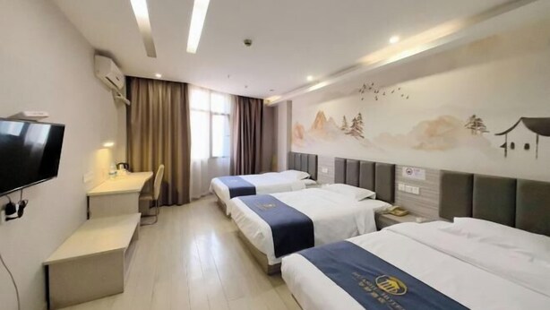 A hotel room with three beds, a desk, a TV, and a mural on the wall. - Thank You Inn (Shanghai Xianghuaqiao) (Shanghai)