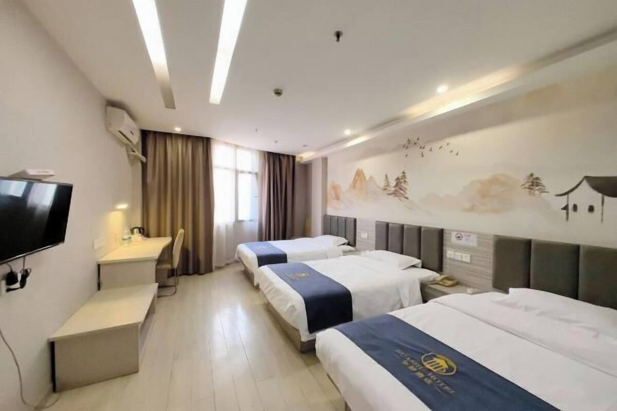 A hotel room with three beds, a desk, a TV, and a mural on the wall.