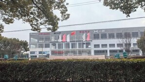 A modern building with multiple flags, a signboard, and a well-maintained hedge in front. - Thank You Inn (Shanghai Xianghuaqiao) (Shanghai)