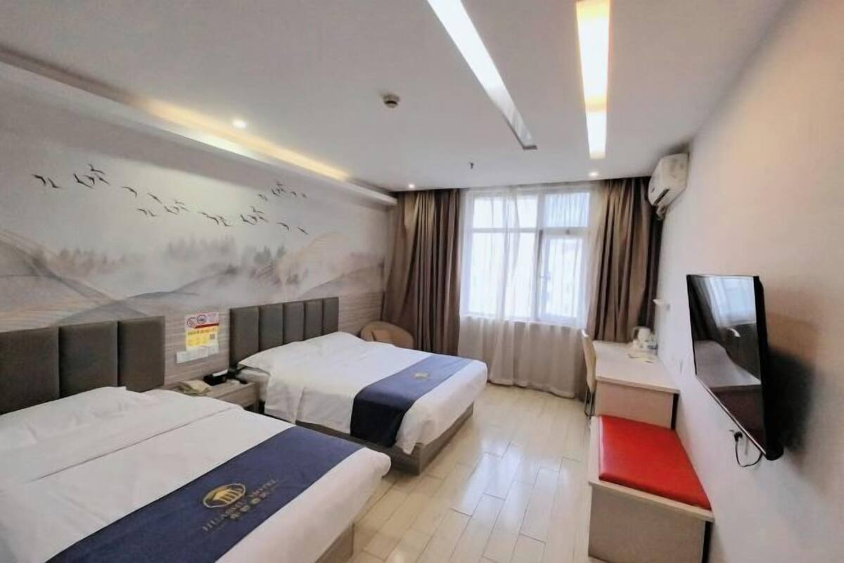 A hotel room with two beds, a desk, a TV, and a mural on the wall.