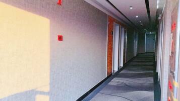 Corredor com piso carpetado, portas à direita e um painel com placas de saída de emergência.