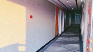 A long, narrow hotel corridor with a carpeted floor, doors on one side, and a plain wall on the other. - Thank You Inn (Shanghai Xianghuaqiao) (Shanghai)