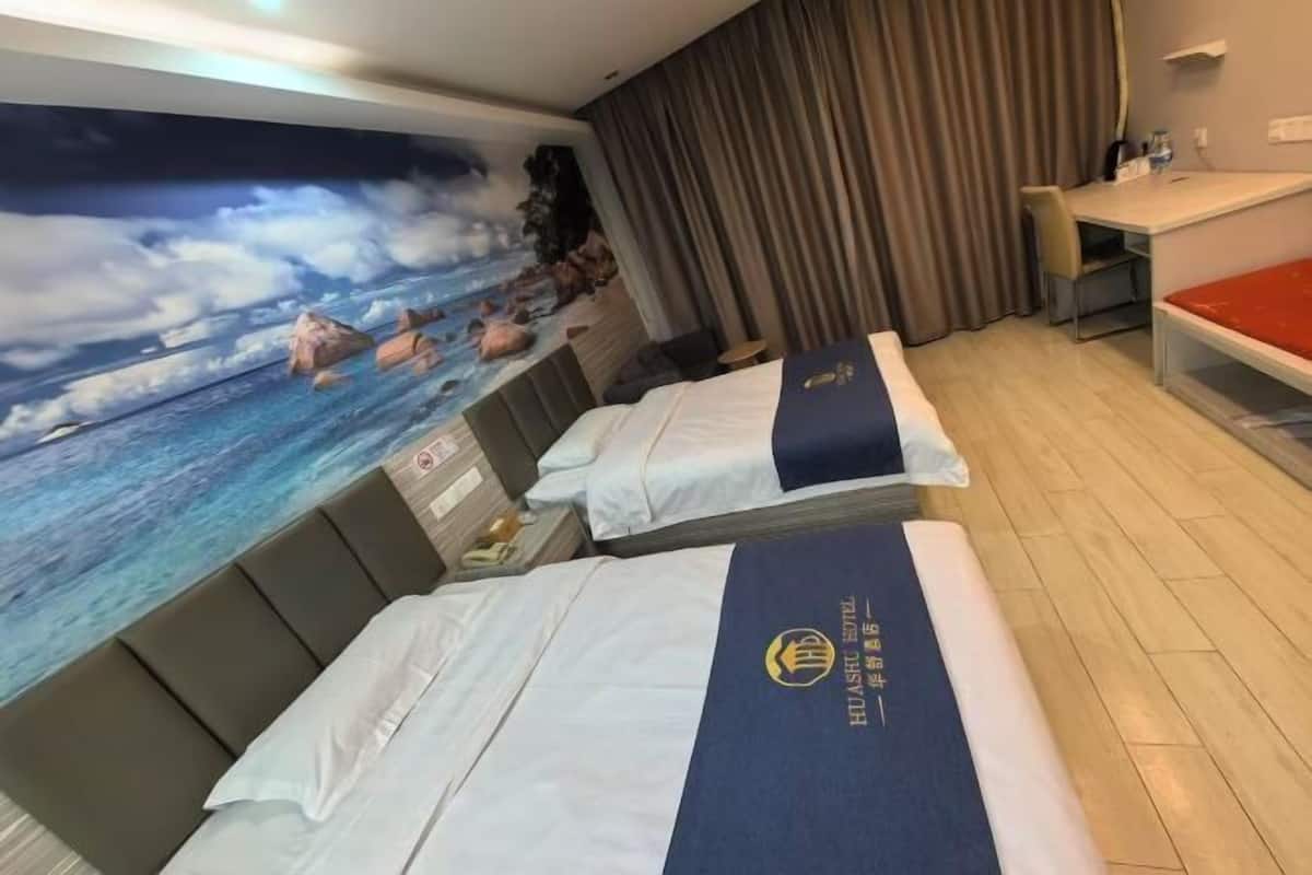 A hotel room with two beds, a desk, a chair, and a large mural of a beach scene.